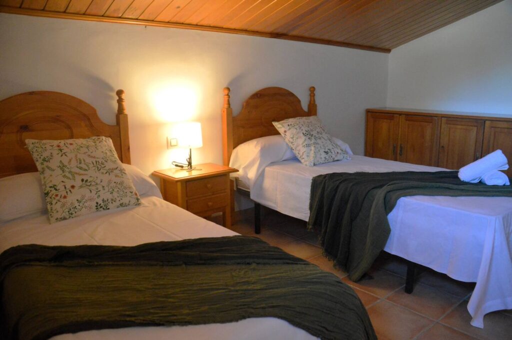 Llit doble amb cobrellit verd, coixins estampats i tovalloles enrotllades.