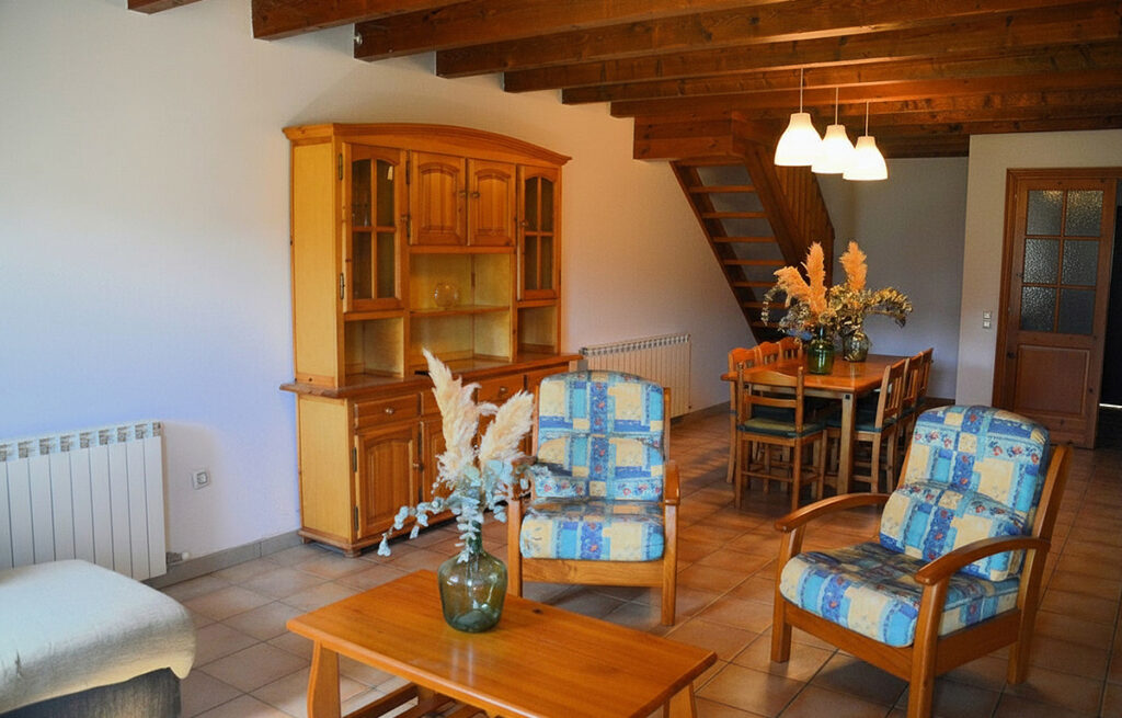 Menjador amb taula de fusta i cadires amb coixins blaus, amb escala de fusta al fons.