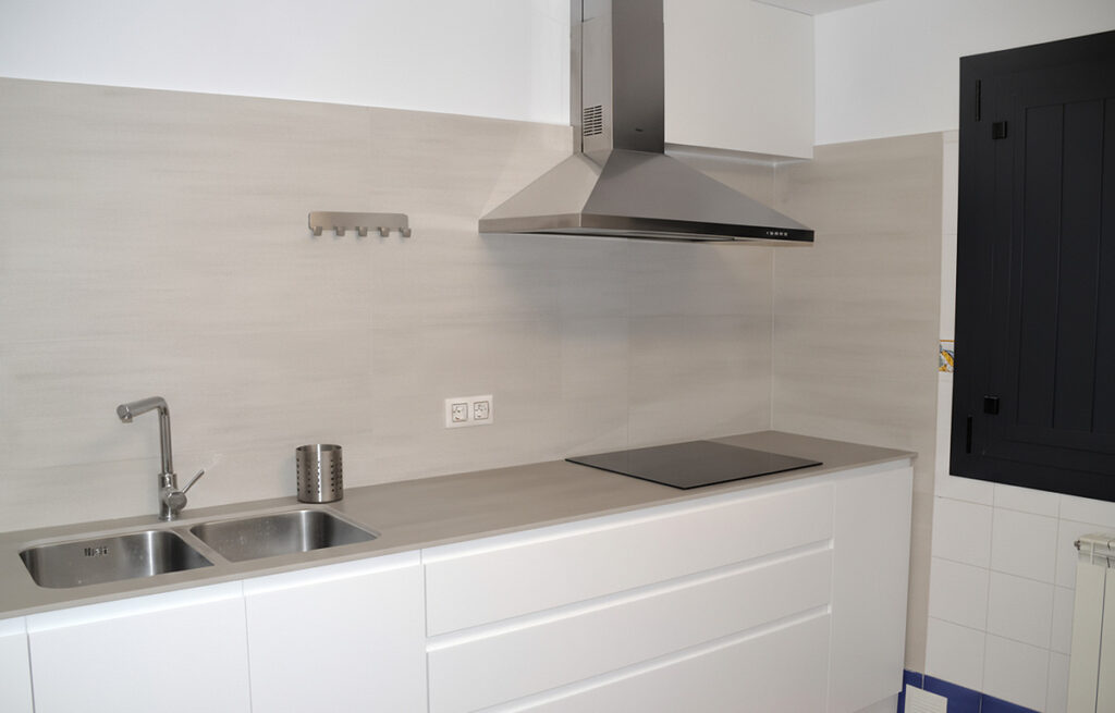 Cuina moderna amb mobles blancs, placa d’inducció i campana d’acer inoxidable.