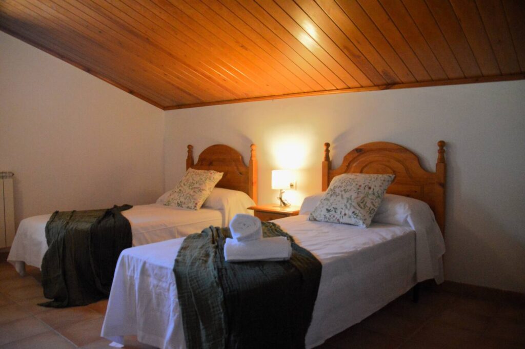 Llit doble amb cobrellit verd, coixins estampats i tovalloles enrotllades.